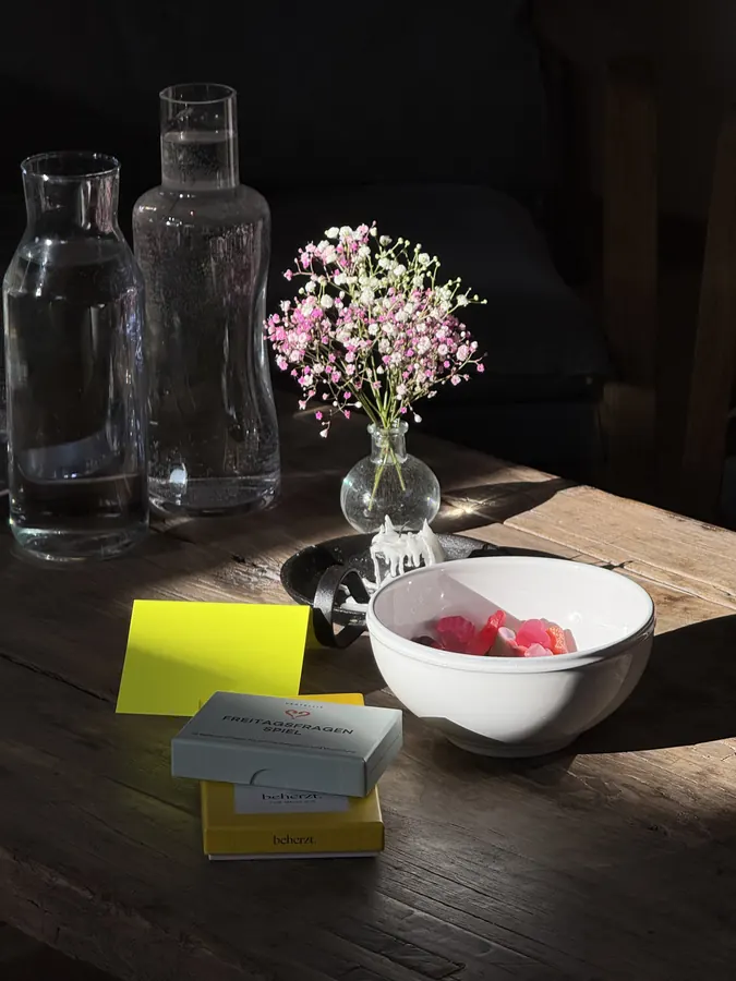 Zwei Glaskaraffen mit Wasser, daneben eine Schale und kleine Blumen auf einem dunklen Holztisch