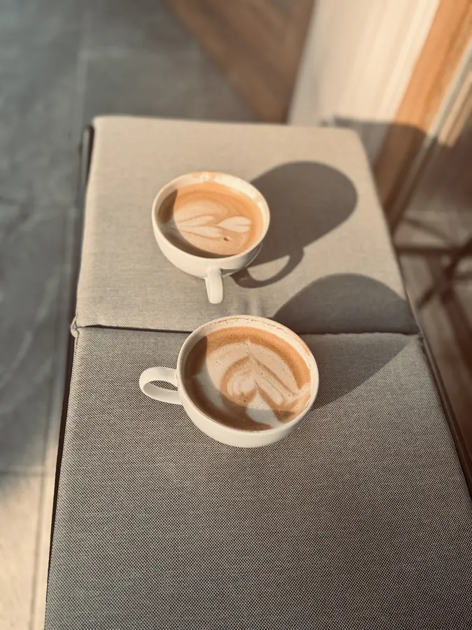 Zwei Cappuccinos mit Latte Art im Morgenlicht auf einer Bank
