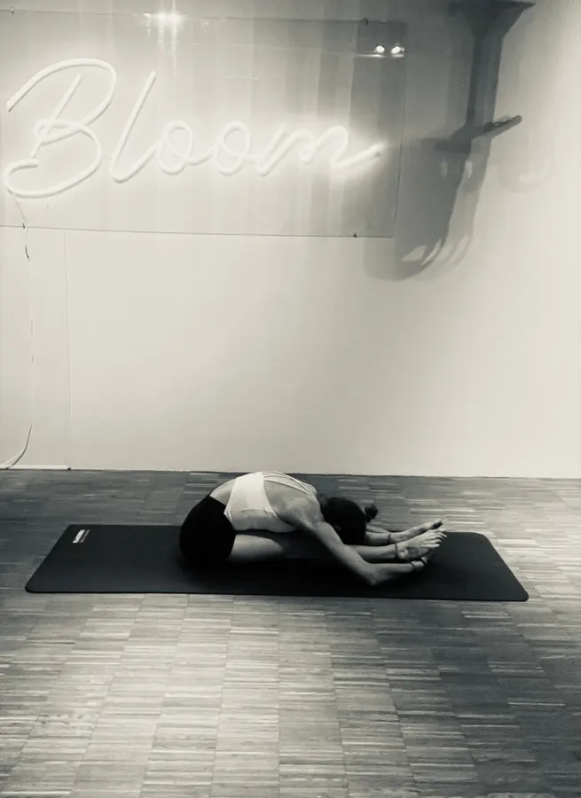 Eine Person in der Kindhaltung auf einer schwarzen Matte vor heller Wand